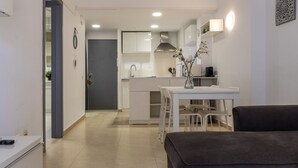 A modern kitchen with white cabinets, a dining table with chairs, and a dark-colored sofa in a bright, well-lit room. - Catalunya 92 by Interhome (Salou)