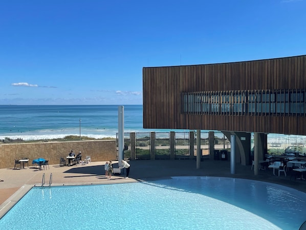 Une piscine avec vue sur lâocĂ©an, un bĂątiment Ă la façade en bois et des espaces de dĂ©tente en plein air.