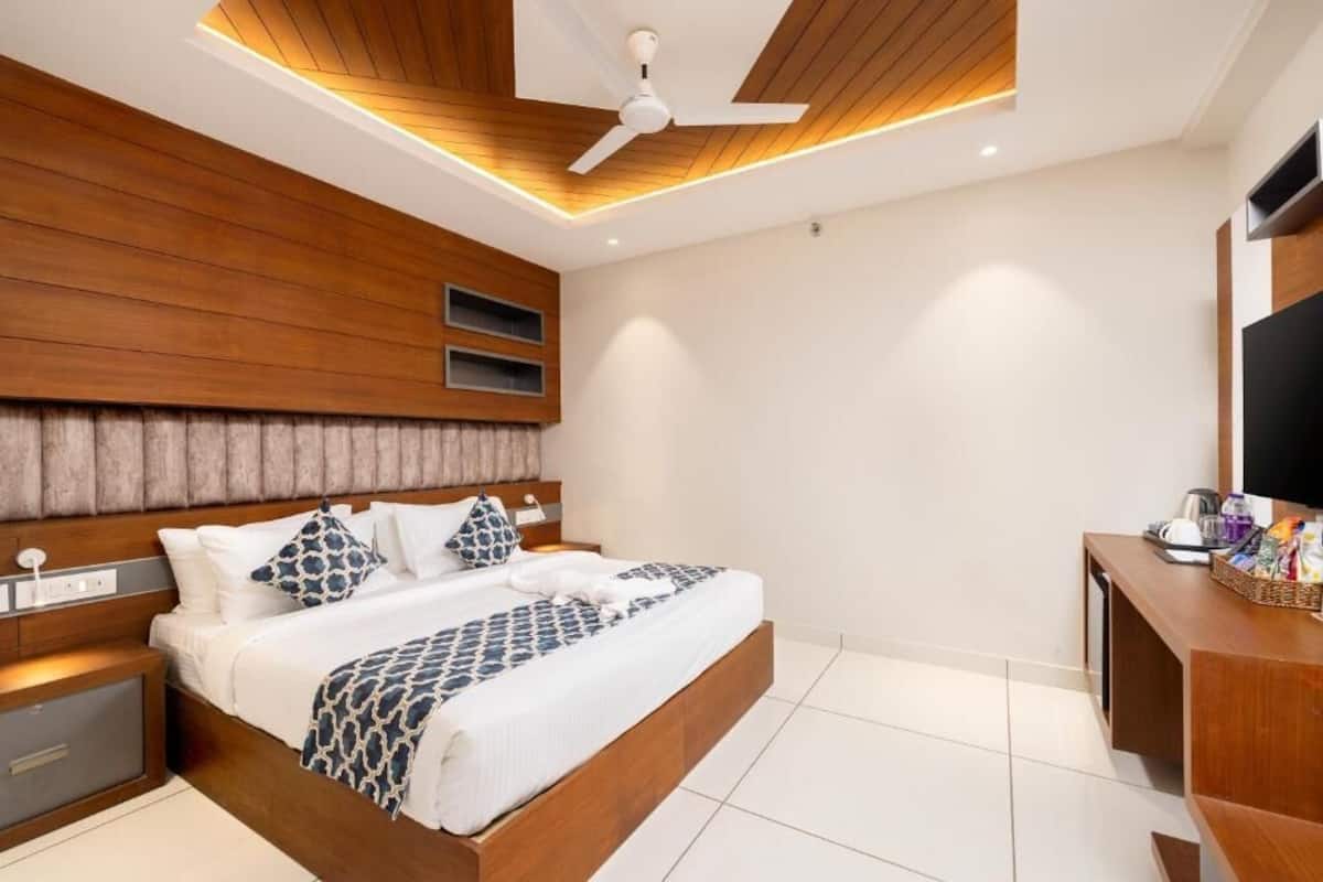 A modern hotel room with a wooden headboard, a bed with patterned bedding, a ceiling fan, and a flat-screen TV on a wooden console.