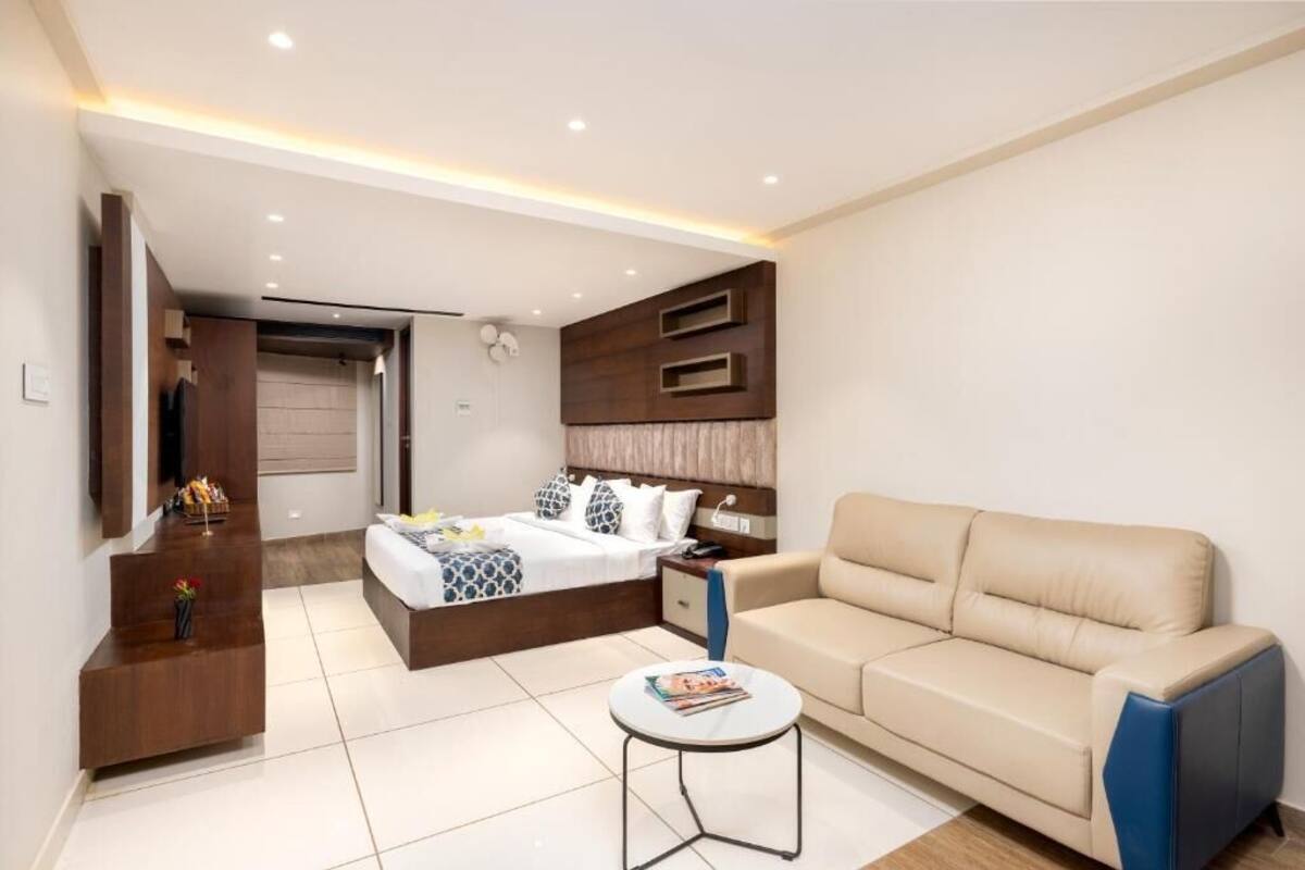 A modern hotel room with a bed, a sofa, a small table, and built-in shelving.