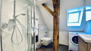 Un baño moderno con ducha de vidrio, una pared de acento de madera, inodoro y lavadora.