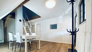 A spacious room with a wooden floor, a white dining table with chairs, a staircase, and a coat rack. - Business Apartment Wangen (Wangen an der Aare)