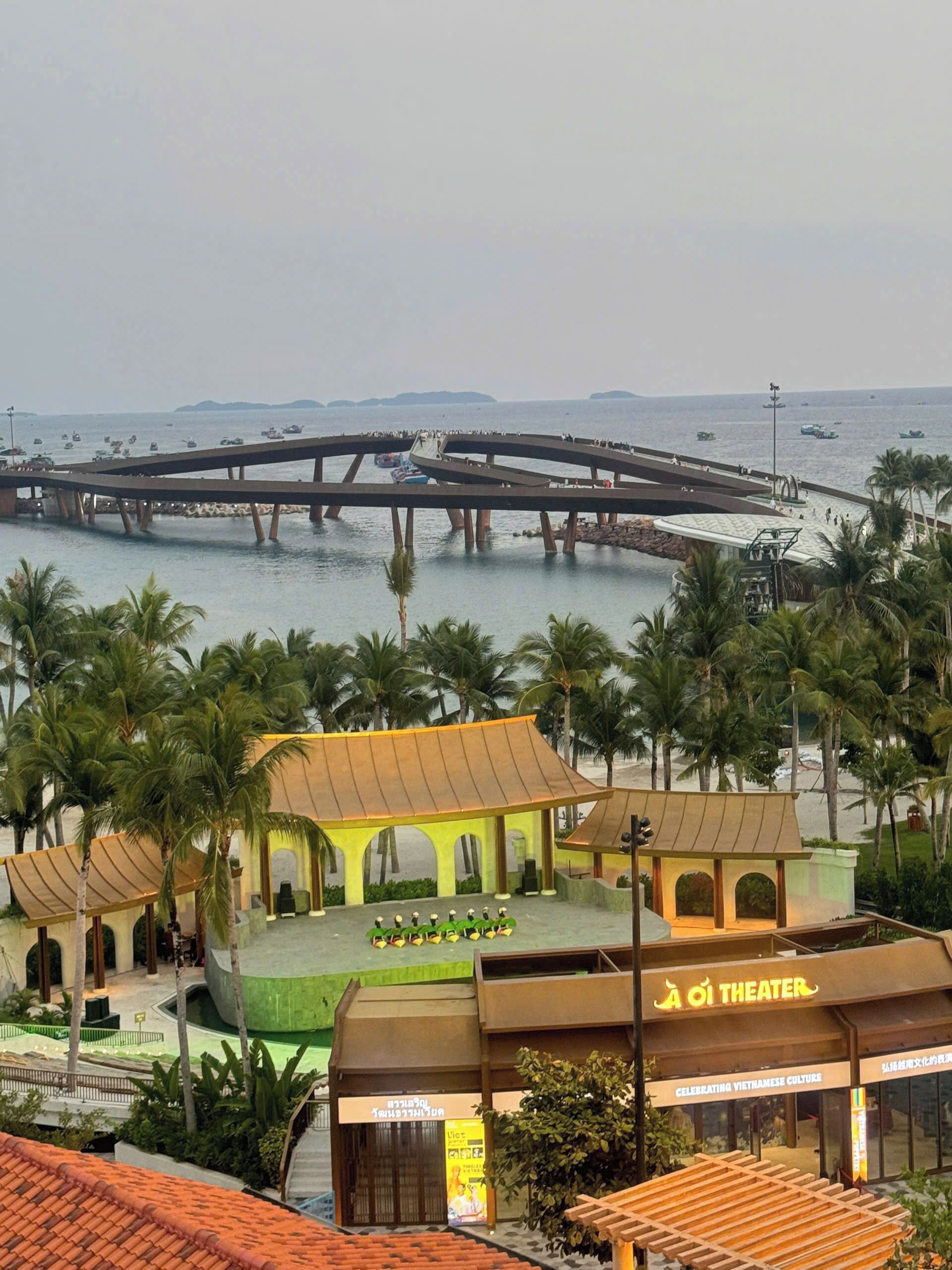 Zona costera con un puente, palmeras y un teatro.