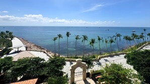 A coastal view with a clear sky, palm trees, and a paved walkway leading to the beach.