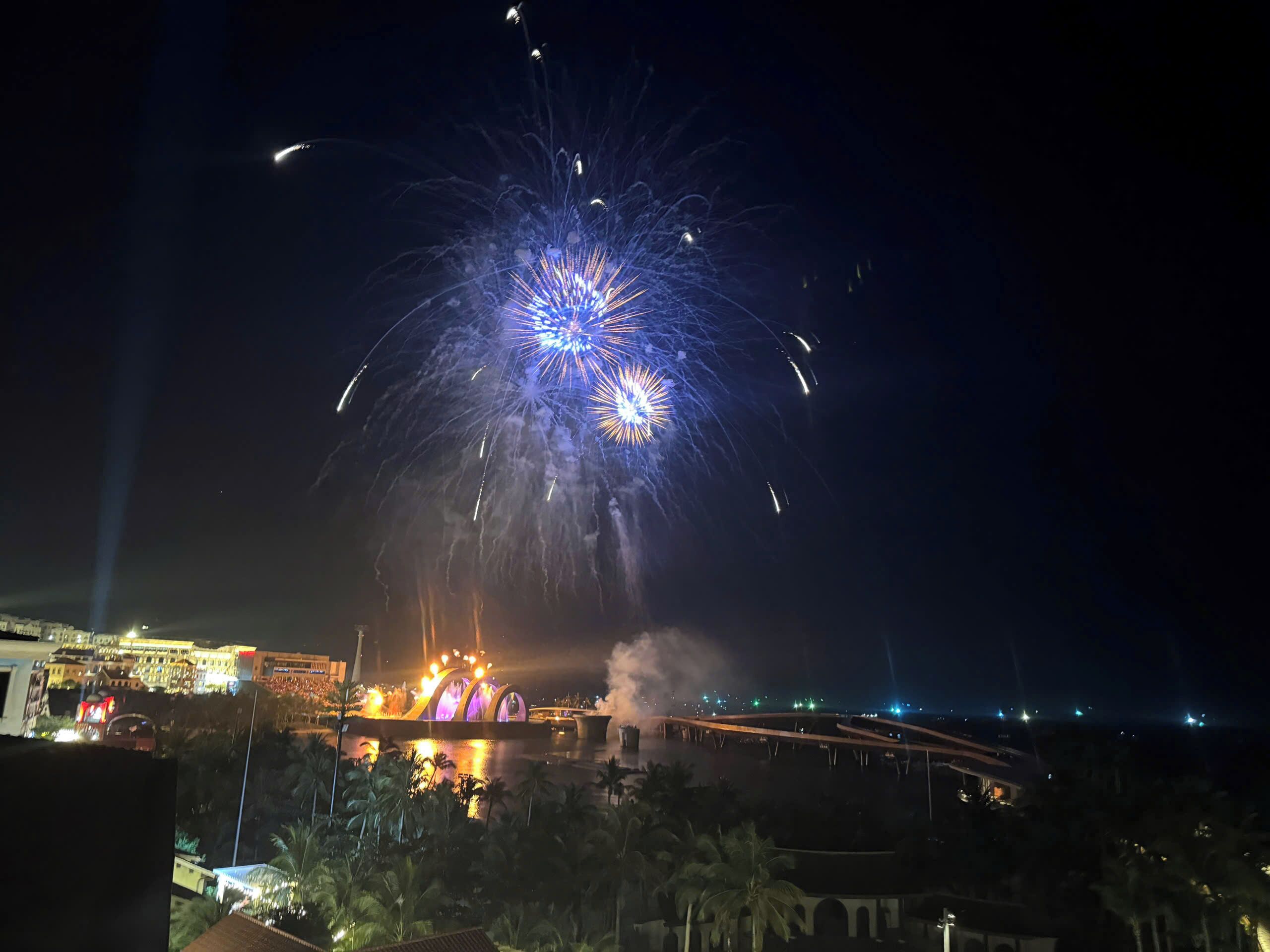 A nighttime view of a cityscape with a prominent bridge and fireworks display.