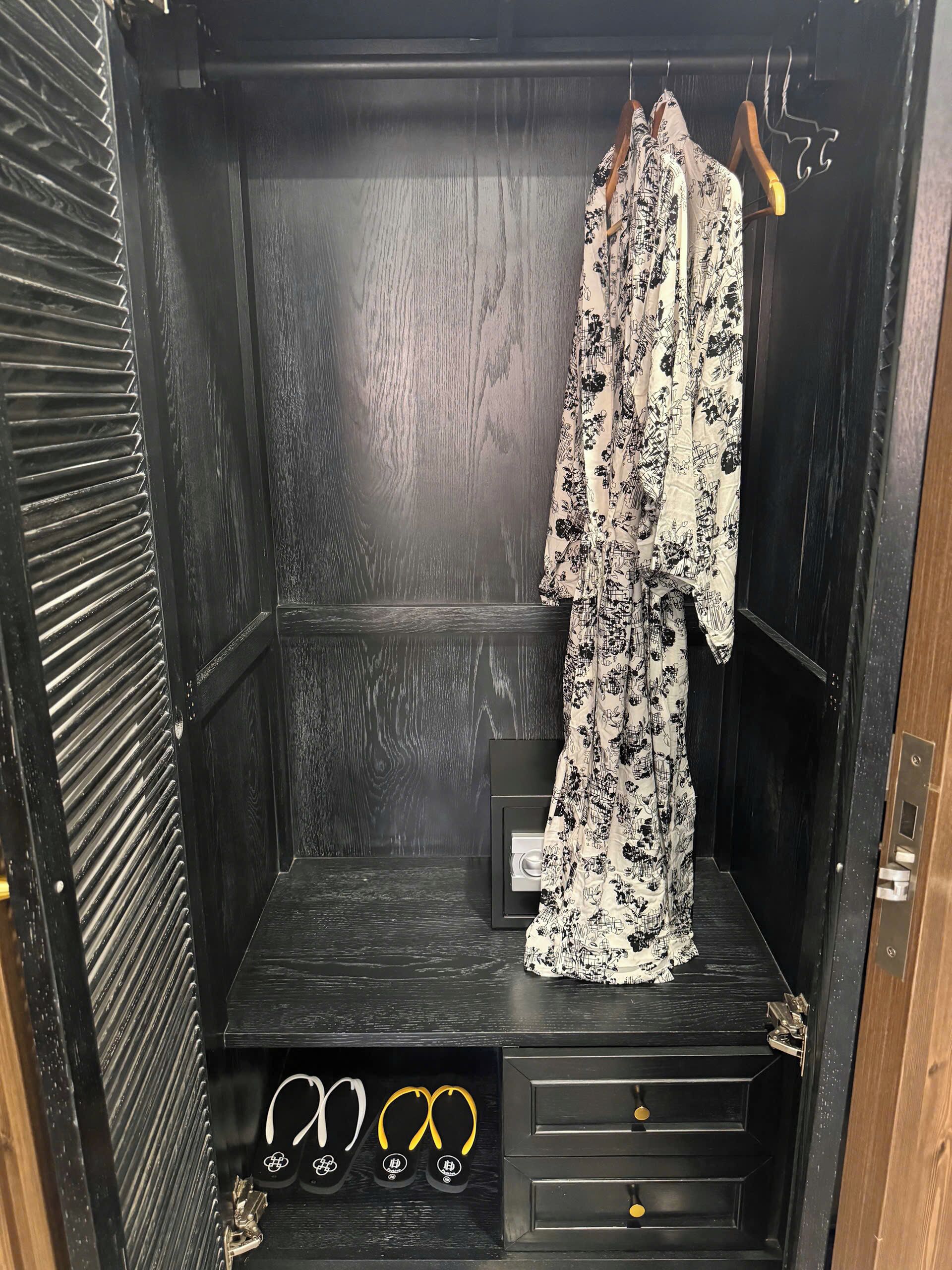 A wardrobe with a black interior, a hanging rack with a floral-patterned garment, and a pair of flip-flops on the lower shelf.