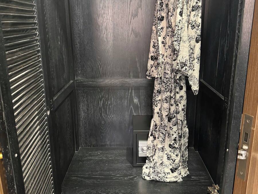 A wardrobe with a black interior, a hanging rack with a floral-patterned garment, and a pair of flip-flops on the lower shelf.