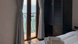 A hotel room with a bed, a large window with curtains, a balcony, and a dark-colored wardrobe.