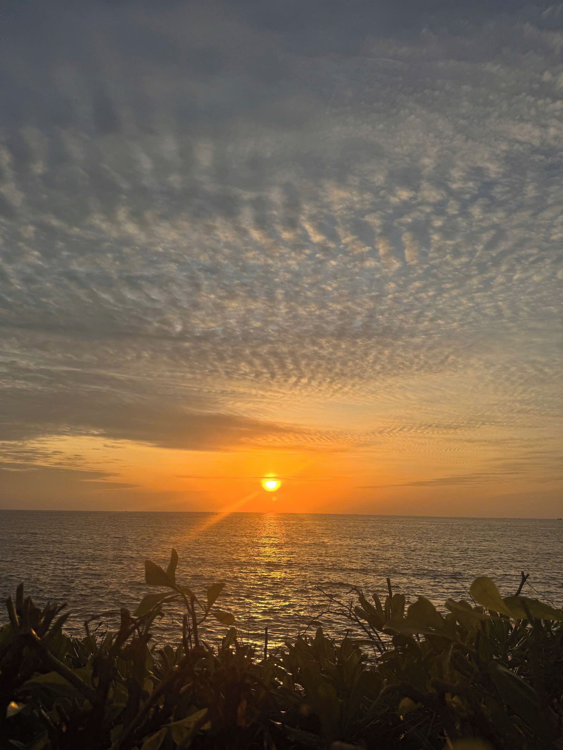 A sunset over a calm sea with a clear sky and some clouds.