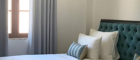 Una habitación de hotel con dos camas, un ventanal con cortinas y un cabecero capitonado.