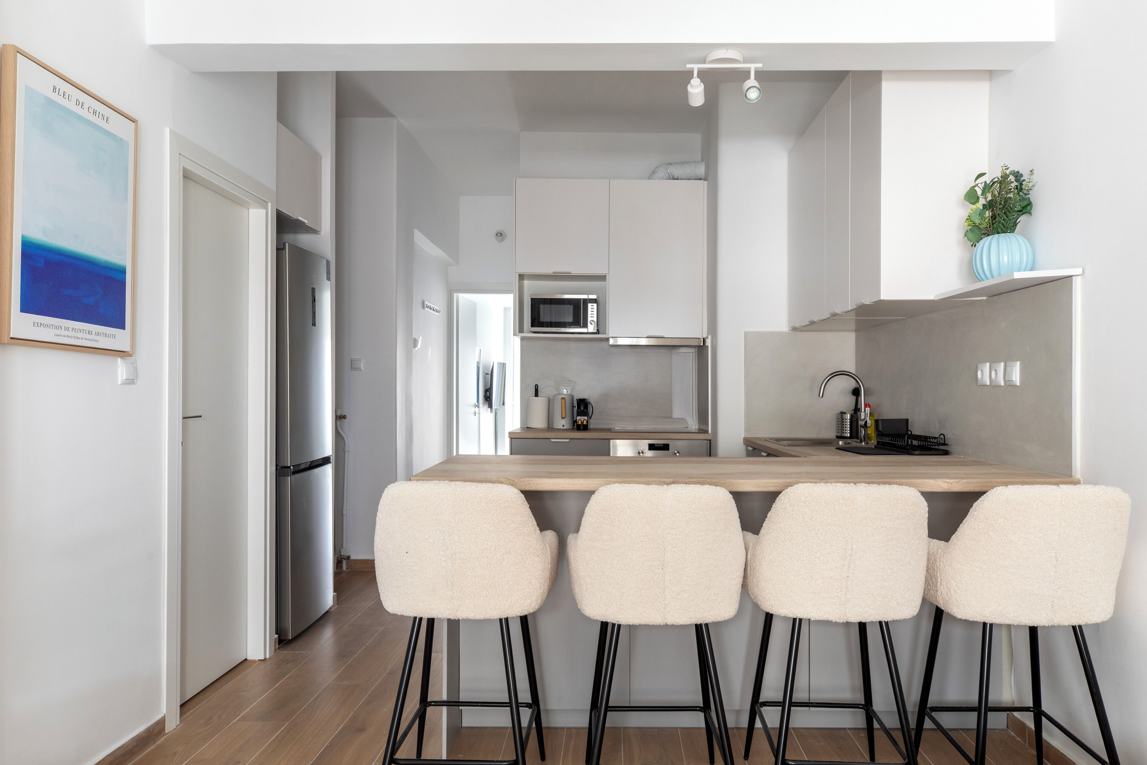 A modern kitchen with a wooden countertop, four bar stools, a microwave, and a stainless steel refrigerator.