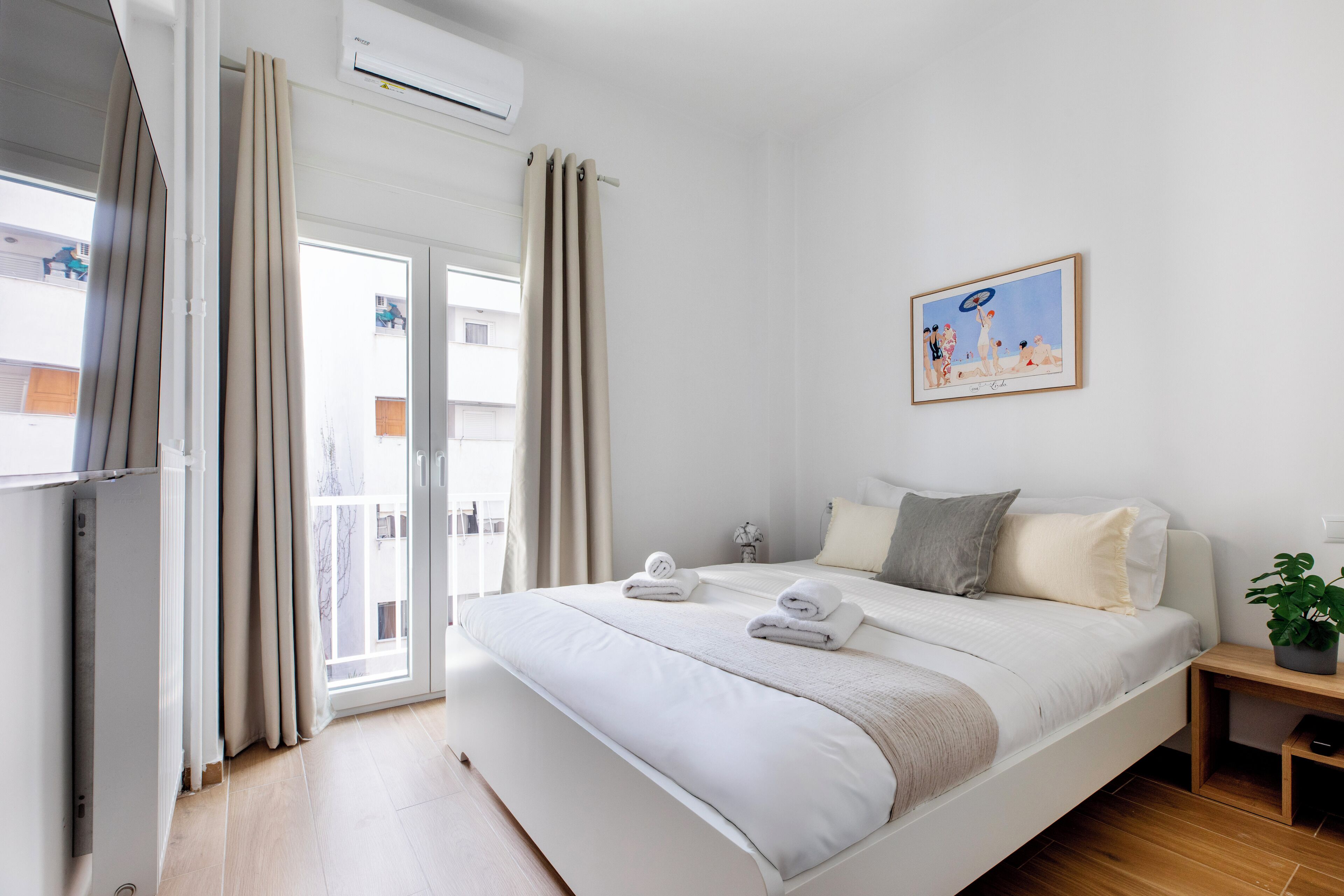 Quarto de hotel moderno com uma cama grande, uma mesinha de cabeceira, uma planta em vaso e uma janela com cortinas.