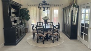 A dining room with a round table, chairs, a chandelier, a cabinet, and a large plant. - Charming 4-br Wine Country Retreat — Walk Downtown Solvang + BBQ & Fireplace (Solvang)