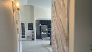 A spacious hallway with a modern kitchen in the background, a large abstract painting on the wall, and a rug leading to the kitchen. - Charming 4-br Wine Country Retreat — Walk Downtown Solvang + BBQ & Fireplace (Solvang)