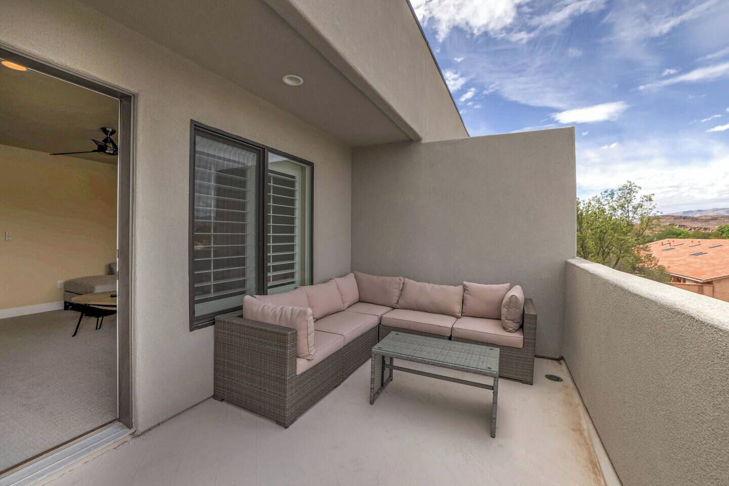 Un balcon avec un canapé d’angle beige, une petite table et une chaise en osier.