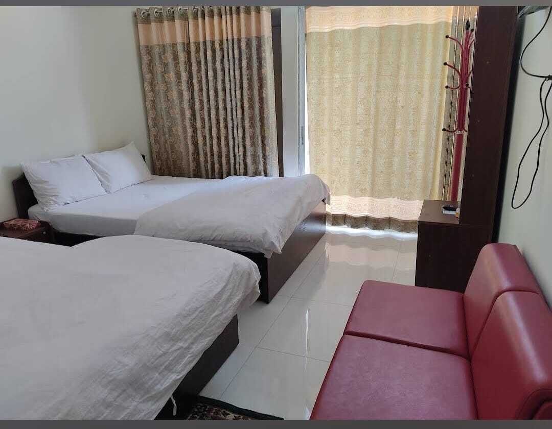 Una habitación de hotel con dos camas, un sofá rojo y un ventanal con cortinas.