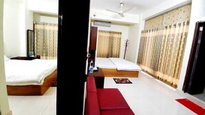 A hotel room with two beds, a red sofa, a ceiling fan, and curtains. - Hotel Grand Valley (Bandarban)