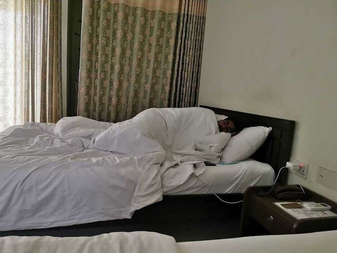 Una habitación de hotel con una cama, una mesita de noche con un teléfono y un libro, y cortinas.