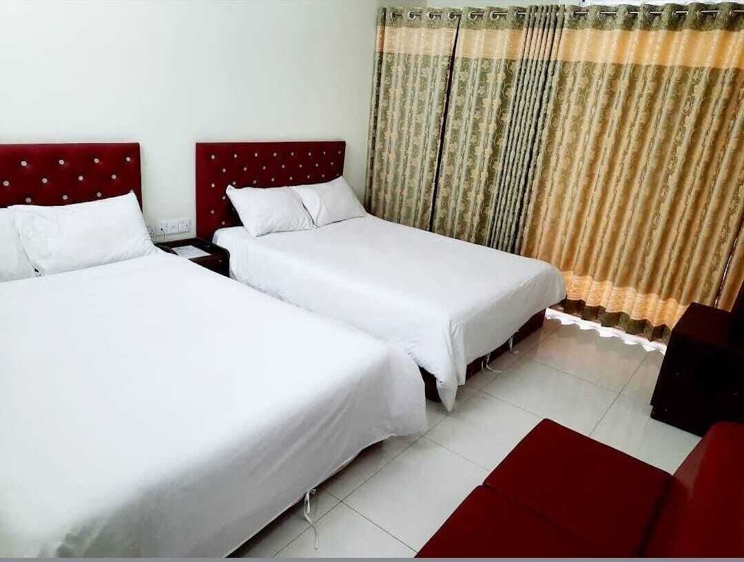 A hotel room with two single beds, a red sofa, and a curtain with a pattern.