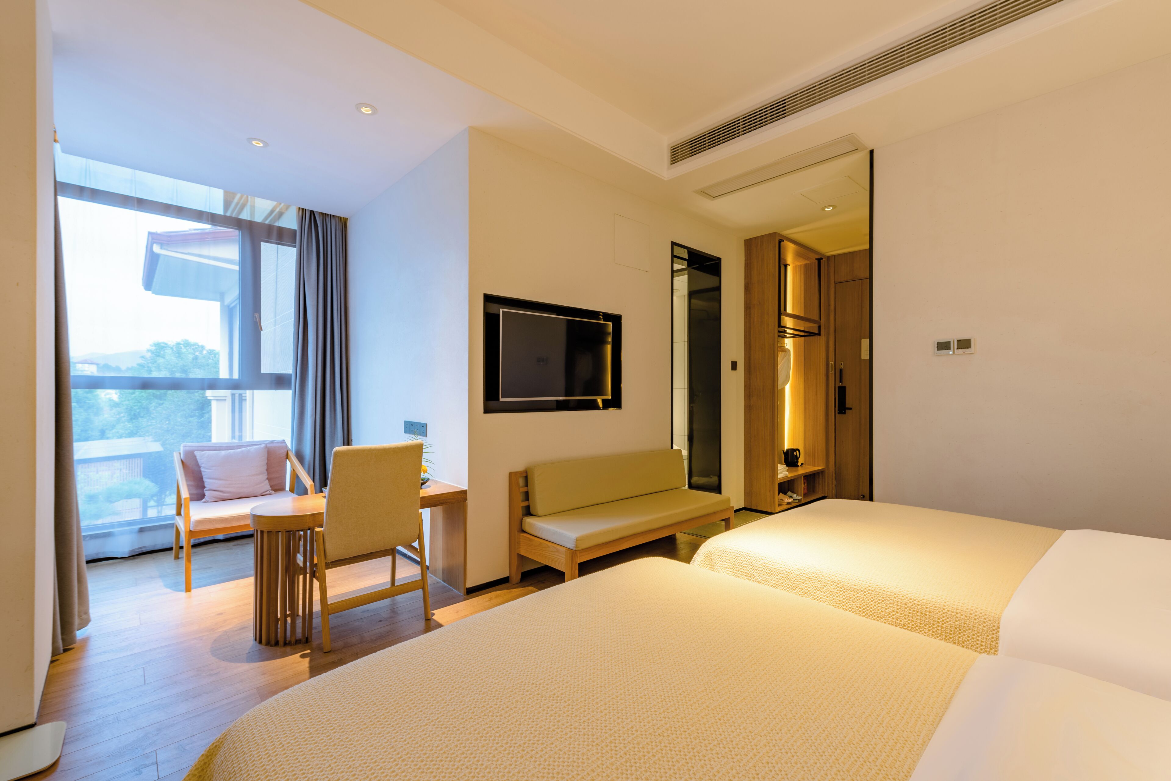 A hotel room with a large bed, a desk with a chair, a sofa, and a TV mounted on the wall.