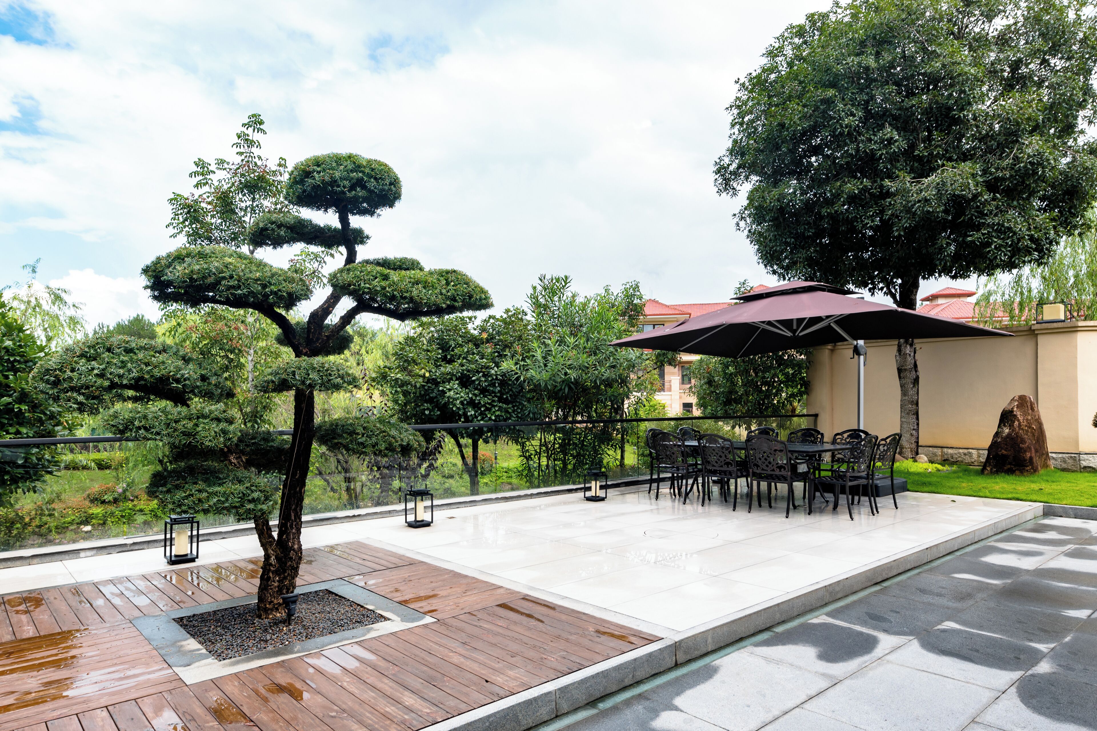 Un espace patio doté d’une terrasse en bois, d’un coin salon avec des tables et des chaises, et d’un grand parasol offrant de l’ombre.