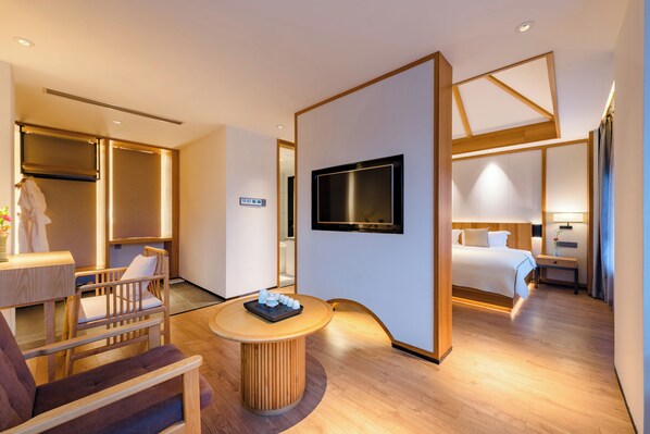 A modern hotel room with a bed, a TV, a seating area with a table, and a wardrobe.