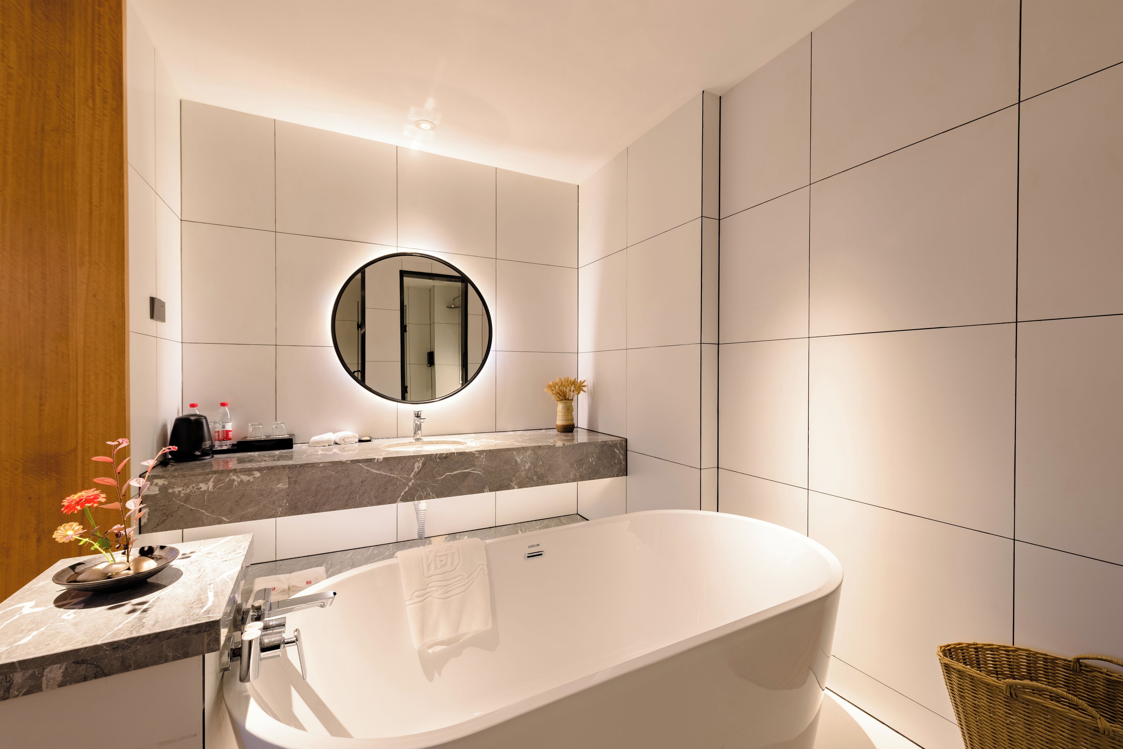 A modern bathroom with a freestanding bathtub, a round mirror, and a marble countertop.