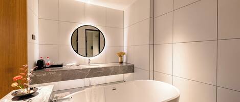 A modern bathroom with a freestanding bathtub, a round mirror, and a marble countertop.