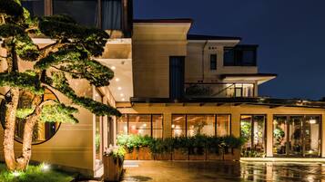 A modern hotel with a spacious outdoor area, a well-lit entrance, and a large tree in the foreground.