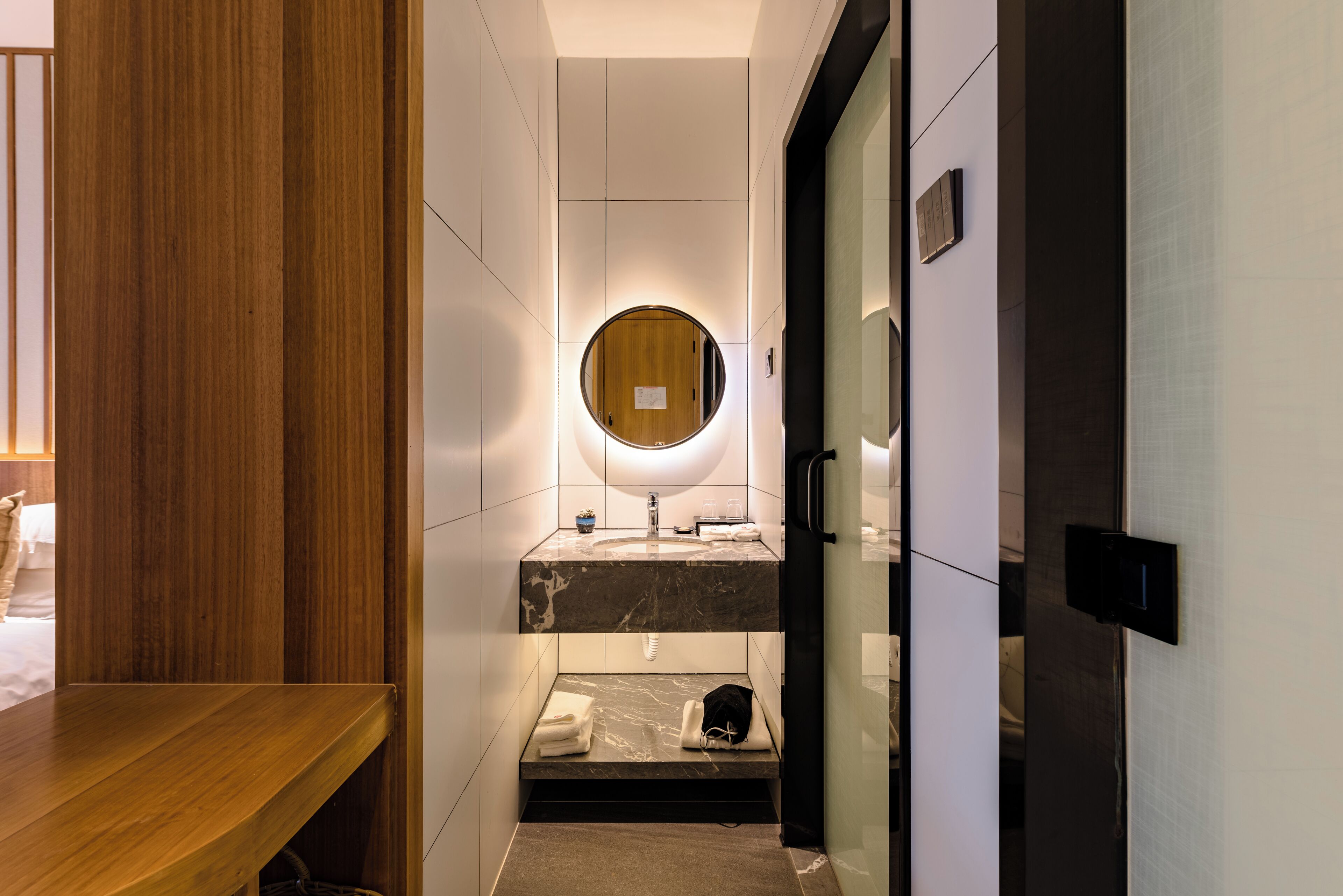 A modern bathroom with a wooden vanity, a round mirror, and a marble sink.