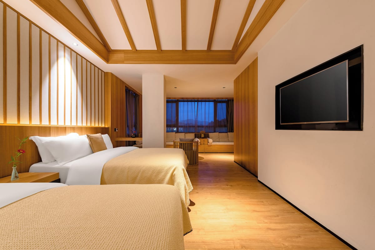 A hotel room with two beds, a TV, wooden paneling, and a view of the night sky.