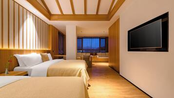 A hotel room with two beds, a TV, wooden paneling, and a view of the night sky.