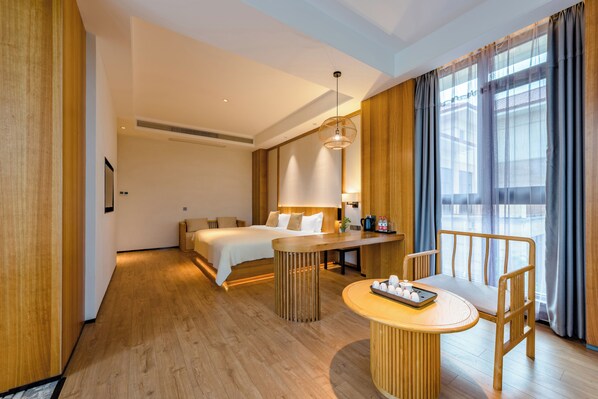 A hotel room with a bed, bedside table, chair, and a small dining table with a tray of items. - Xi He Yuan (Nanping)
