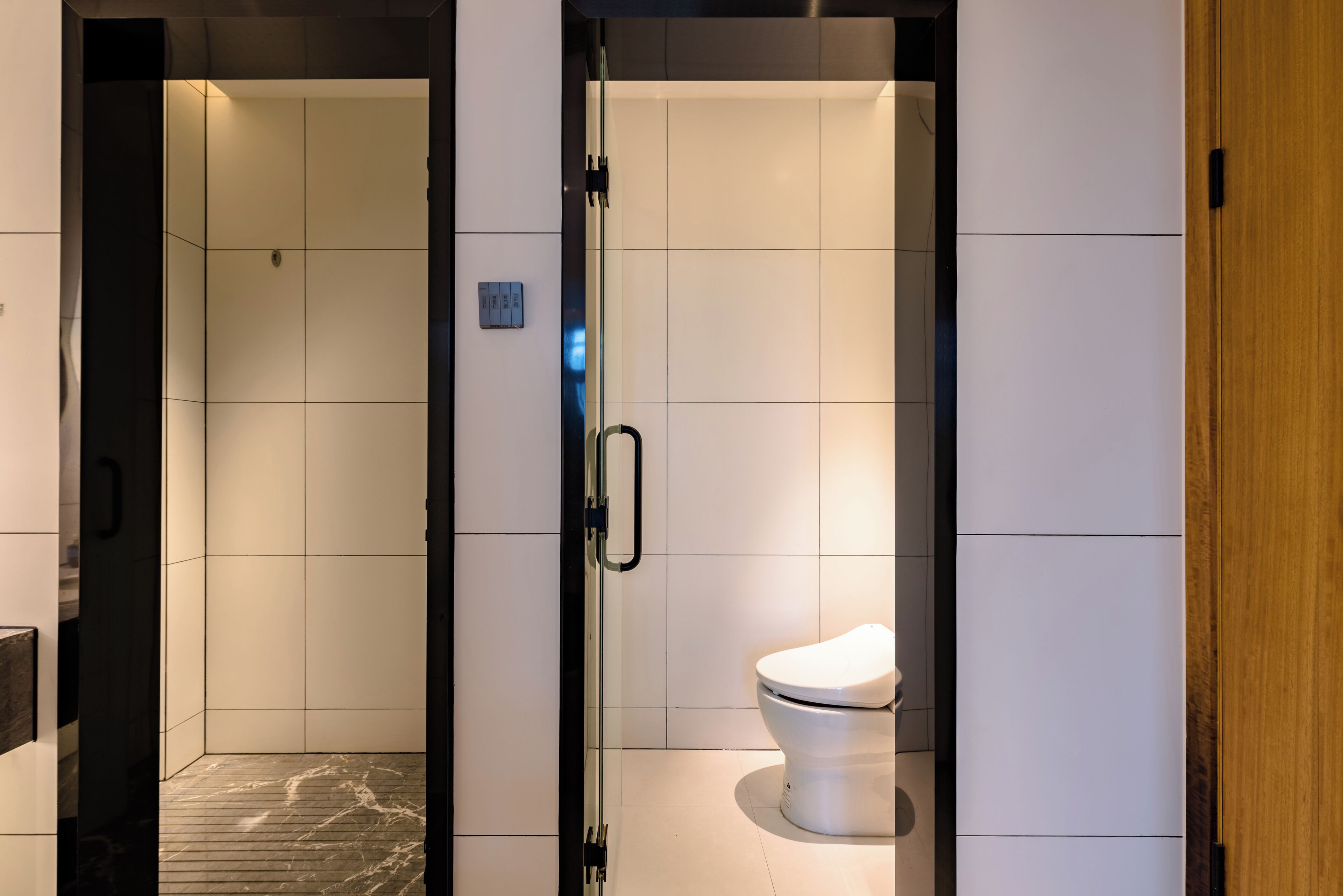 Um banheiro moderno com divisória de vidro, vaso sanitário branco e piso revestido de azulejos.