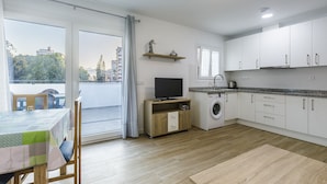 Una cocina moderna con lavadora incorporada, un comedor con mesa y sillas, y un balcón con vistas a la ciudad.