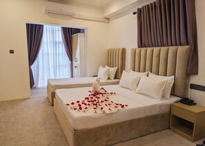 A hotel room with two beds, a large window with curtains, an air conditioning unit, and a bedside table with a phone. - Kings Grand Hotel (Colombo)