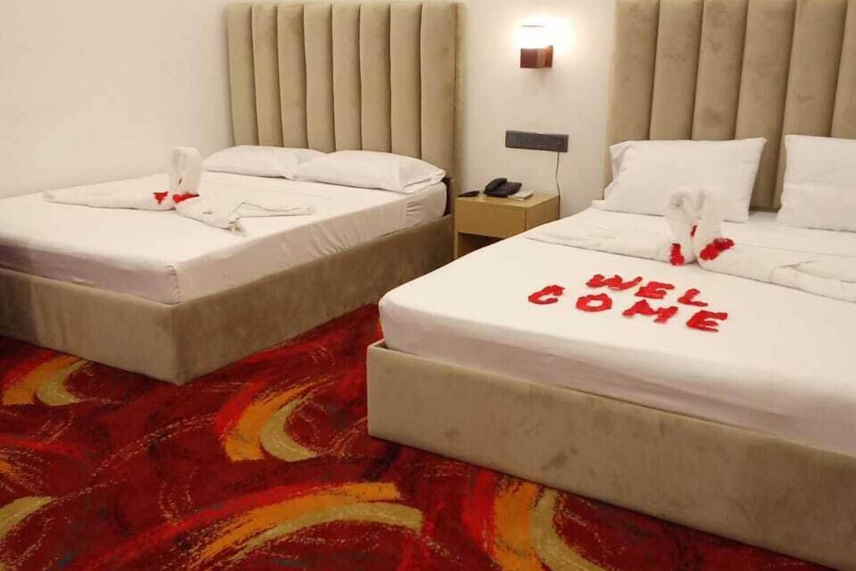 Two twin beds with a red "WELCOME HOME" sign on the bedspread, a beige headboard, and a patterned carpet.
