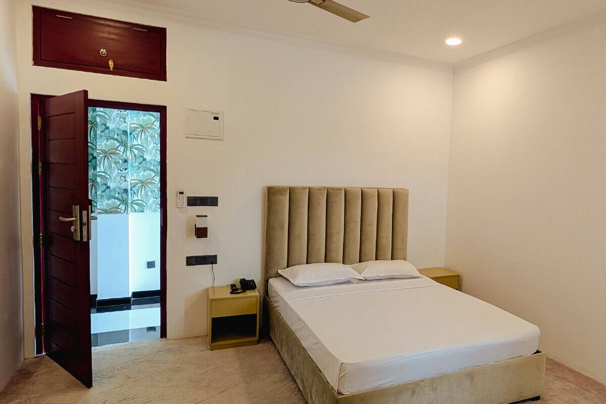 A bedroom with a bed, a nightstand, a bedside table, a ceiling fan, and a door leading to another room.