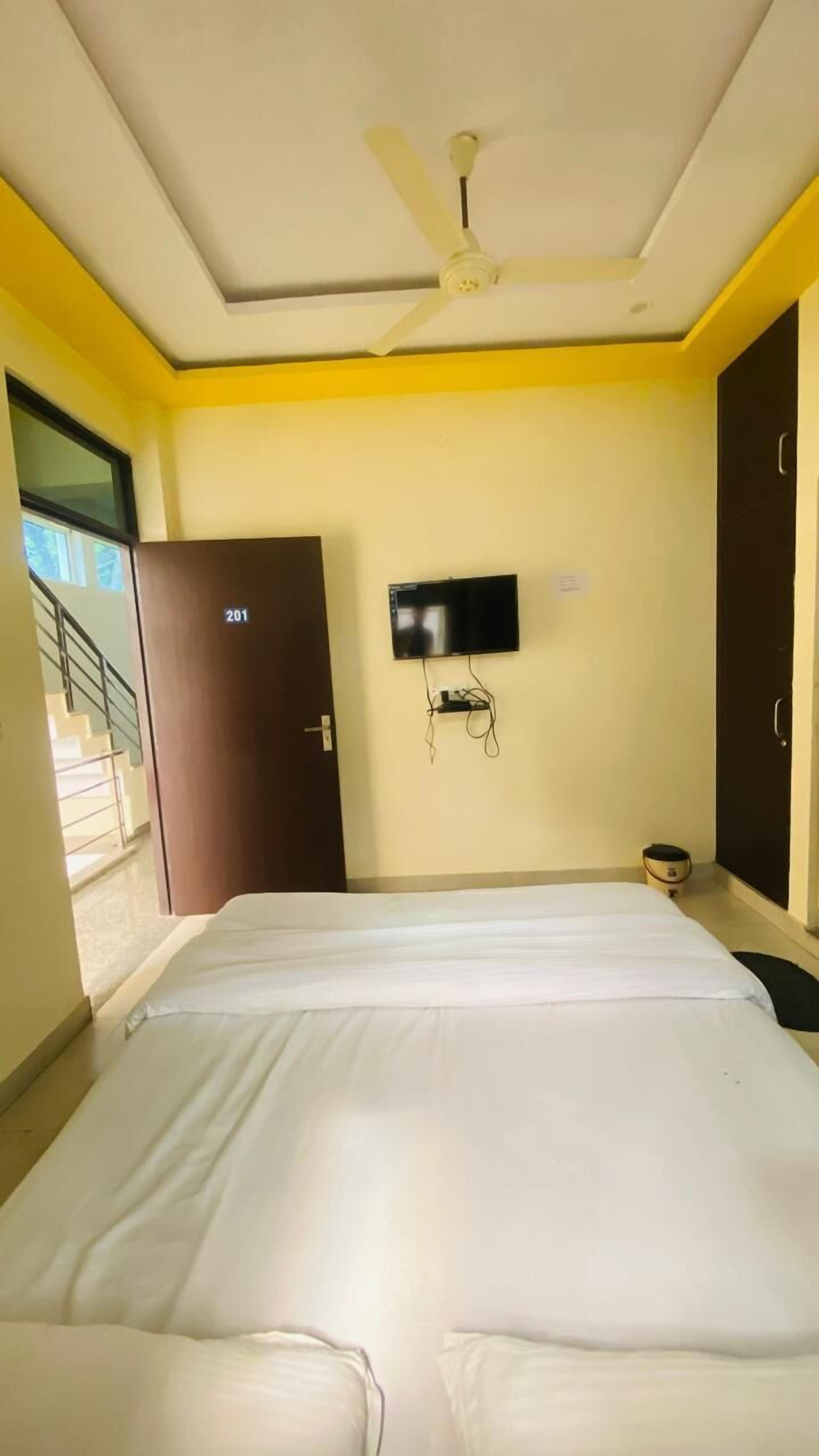 Ein Hotelzimmer mit Bett, Deckenventilator, an der Wand montiertem Fernseher und einer Tür mit Hinweisschild.