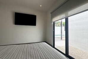 A bedroom with a bed, a TV mounted on the wall, and a sliding glass door leading to an outdoor area.