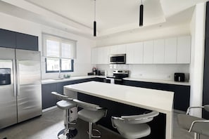 A modern kitchen with a central island, bar stools, stainless steel appliances, and white cabinetry.