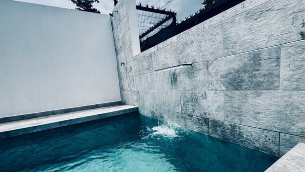 A swimming pool with clear water, surrounded by stone walls and a white structure. - Ocean Villas Modern Home w/ Pool (Coco)