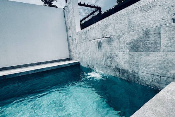 A swimming pool with clear blue water, surrounded by stone walls and a white fence.