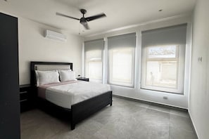 Ein Schlafzimmer mit Bett, Deckenventilator und großen Fenstern.