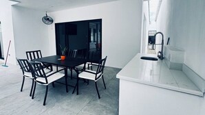 A modern kitchen with a white countertop, a dining table with chairs, and a large window. - Ocean Villas Modern Home w/ Pool (Coco)