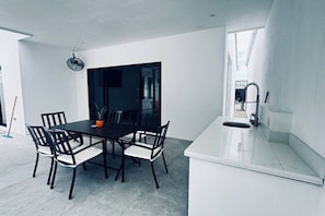 A modern kitchen with a white countertop, a dining table with chairs, and a large window.