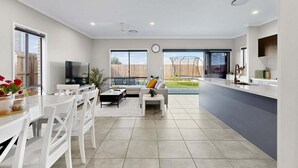 A modern living room with a sofa, coffee table, and TV. There is a kitchen area with a counter and cabinets. - Griffin Family Stay – 4BR Modern Home (Griffin)