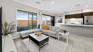A modern living room with a sofa, coffee table, and a view of a backyard. - Griffin Family Stay – 4BR Modern Home (Griffin)