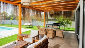 Un patio couvert avec des meubles en bois, une piscine et un espace barbecue.