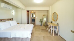 Une chambre d’hôtel avec un grand lit, un bureau, une chaise, un miroir et une salle de bain visible à travers une porte ouverte.